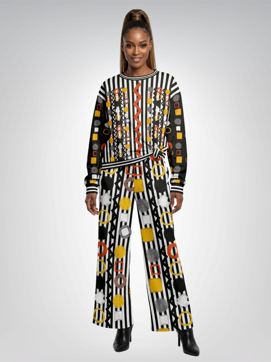 A woman modeling a long-sleeve sweatshirt and wide leg pants with a bold geometric pattern in black, white, yellow, orange, and gray, set against a plain light gray studio background.