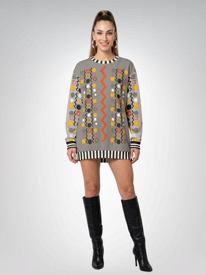 A woman modeling a gray long-sleeve sweatshirt worn as a mini dress with colorful geometric patterns and black striped trim, paired with black knee-high boots, against a light gray studio background.