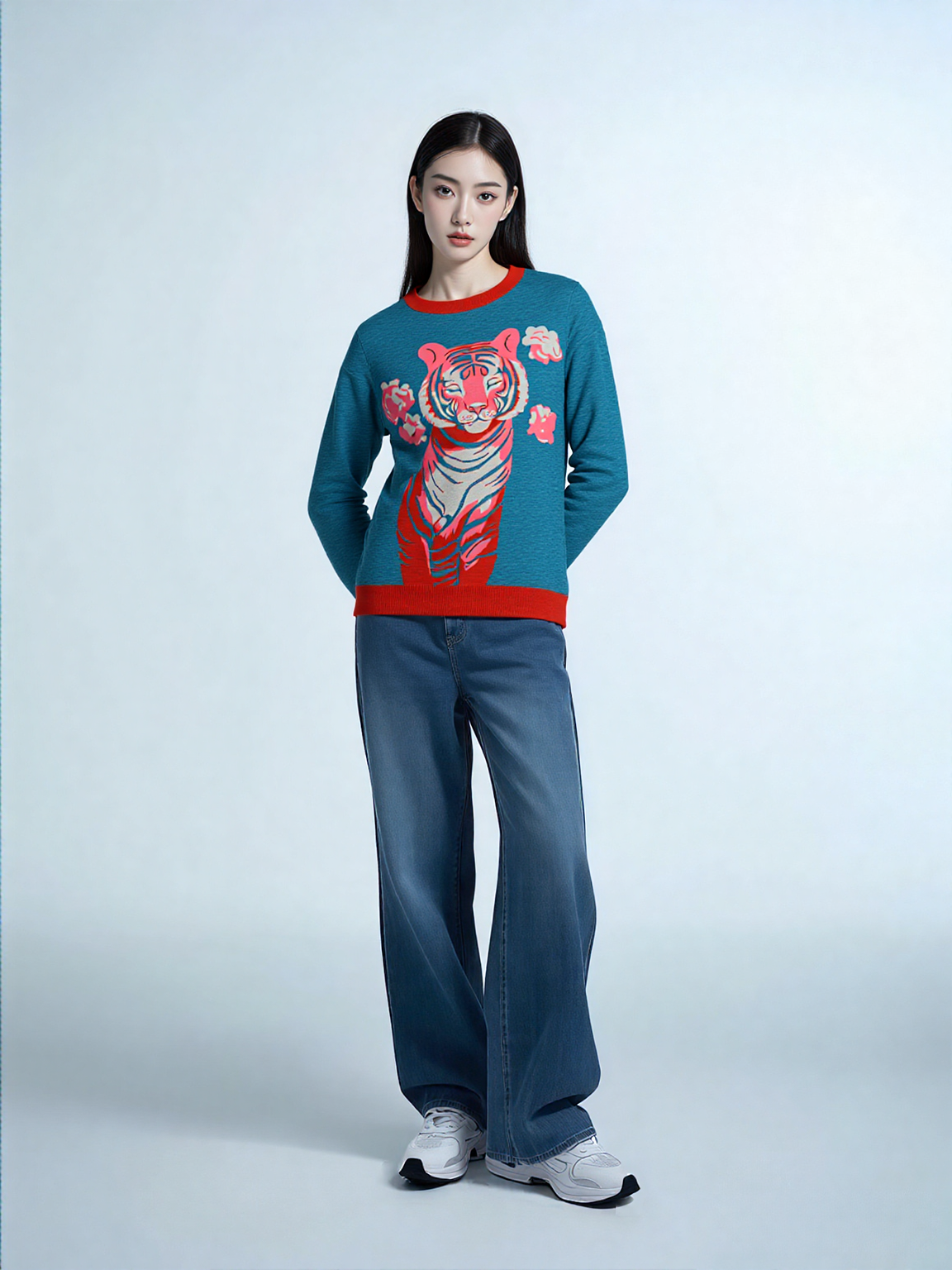 Person wearing a blue sweater with a tiger design and blue jeans on a white background
